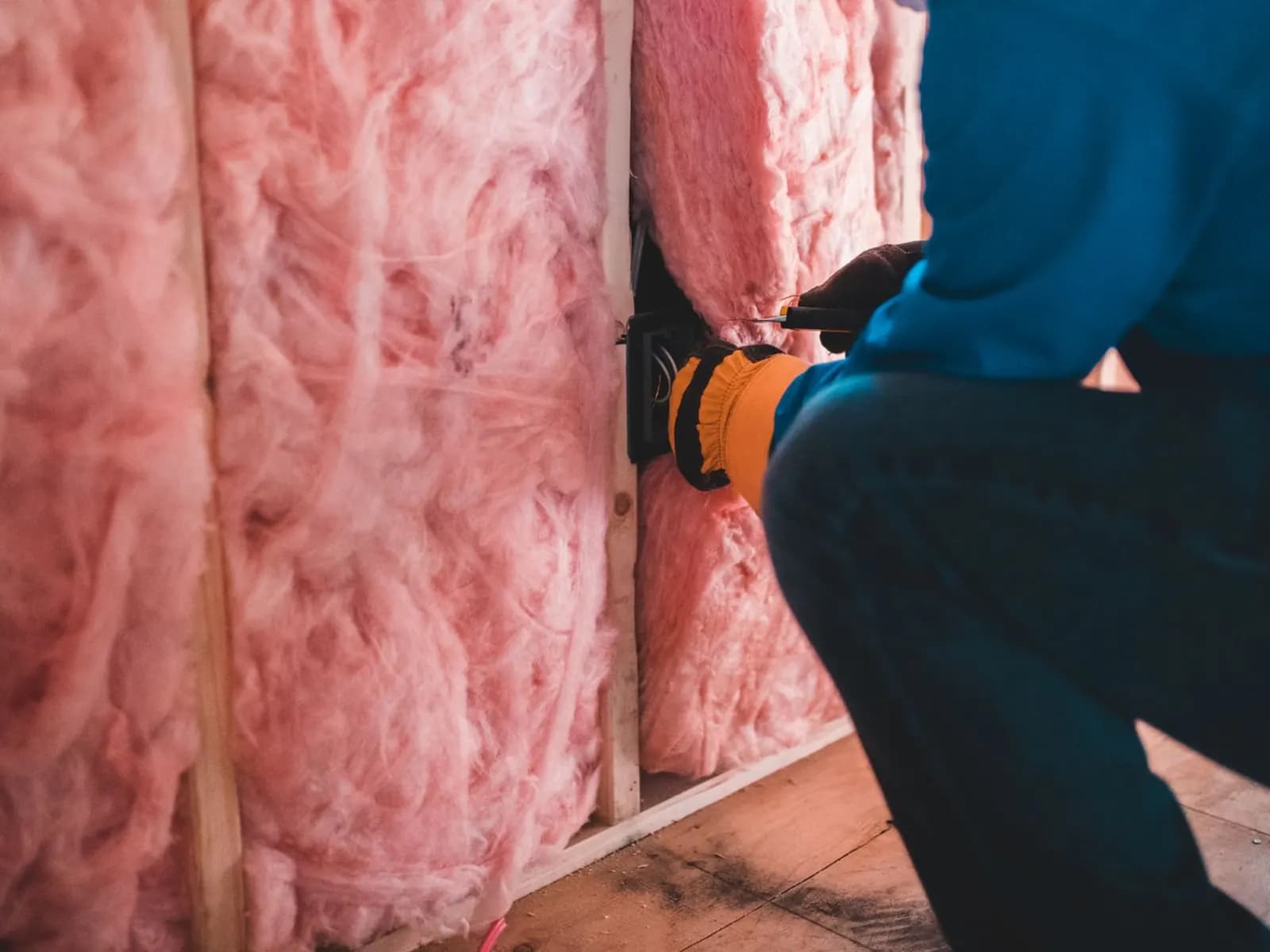 Installer fitting pink batt insulation between the studs of a timber-framed wall