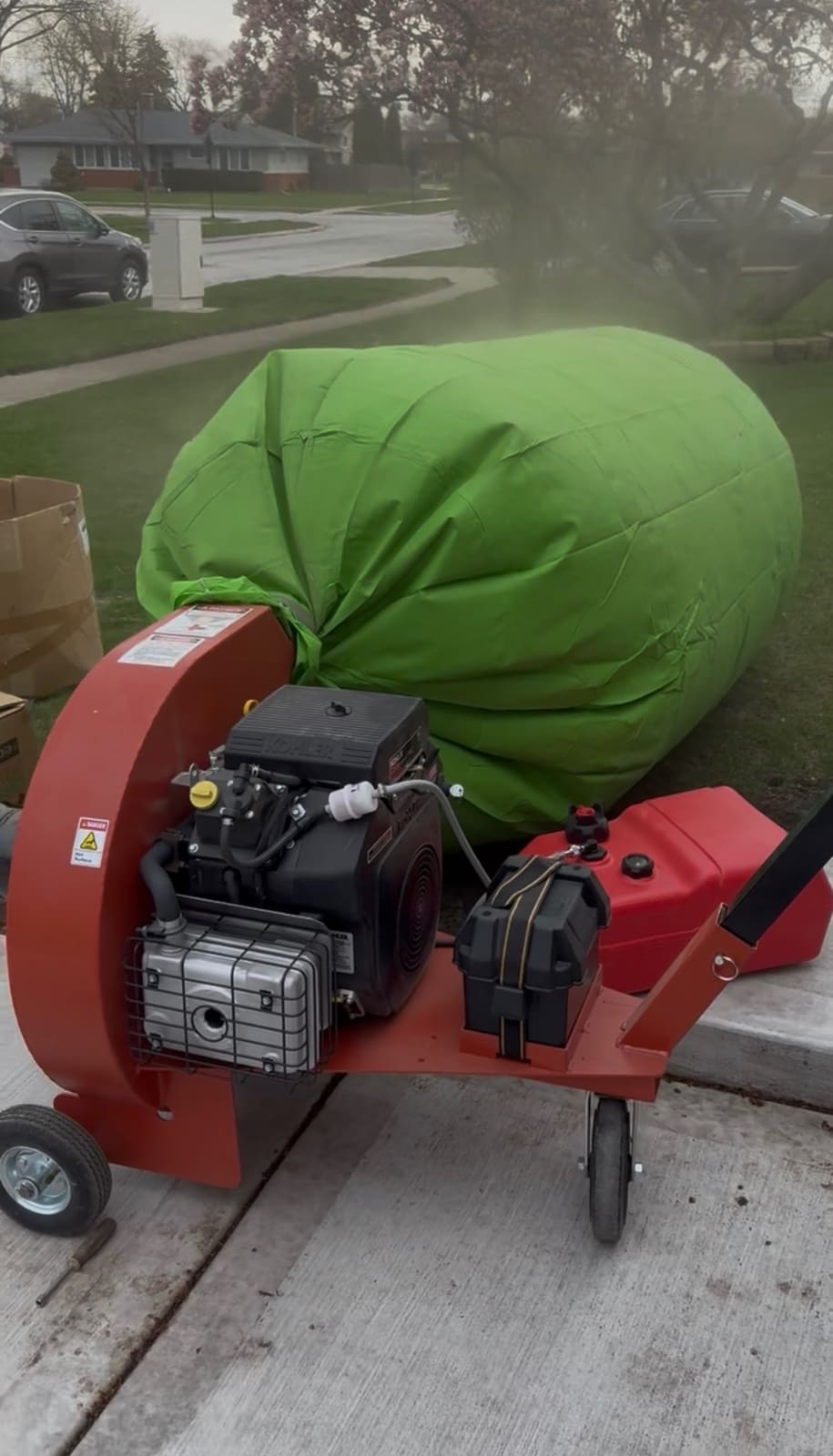 Gas powered insulation removal vacuum and a filled green disposal bag set up on the driveway of a home in Kane County, IL during an attic insulation removal