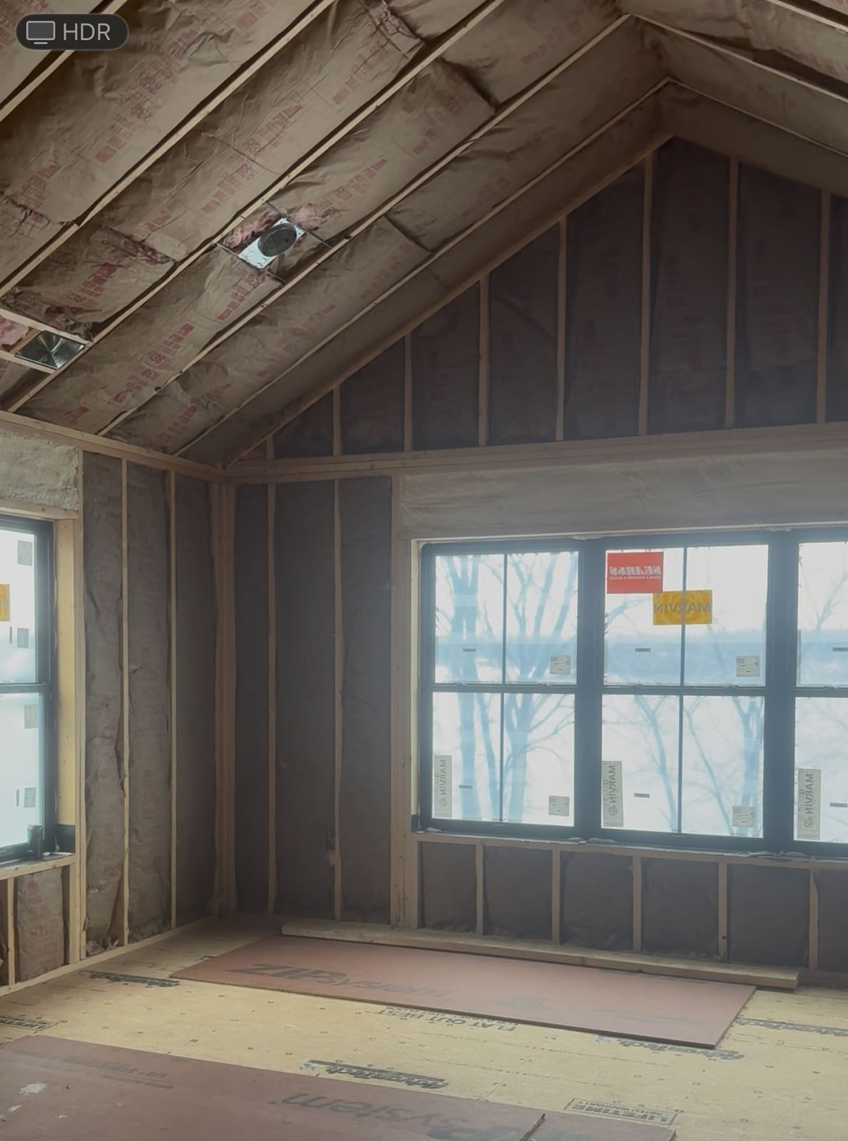 Kraft faced fiberglass batt insulation between the rafters of a cathedral ceiling and in the gable end wall of a newly framed room near Elgin, IL, with a bank of windows looking out onto snow