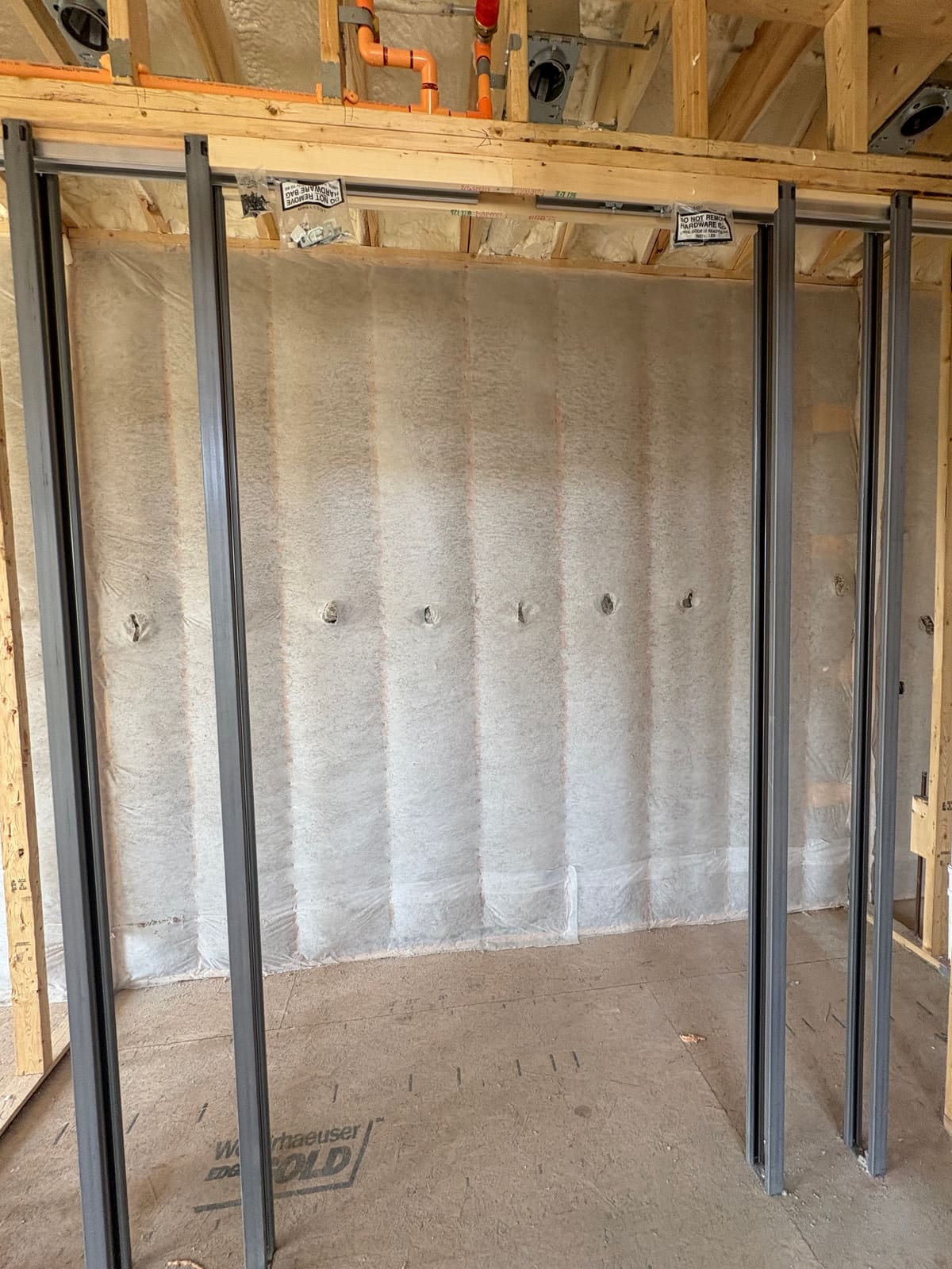 Fiberglass insulation packed into the stud cavities of an interior wall and held in place behind netting, with steel pocket door frames standing in front of it