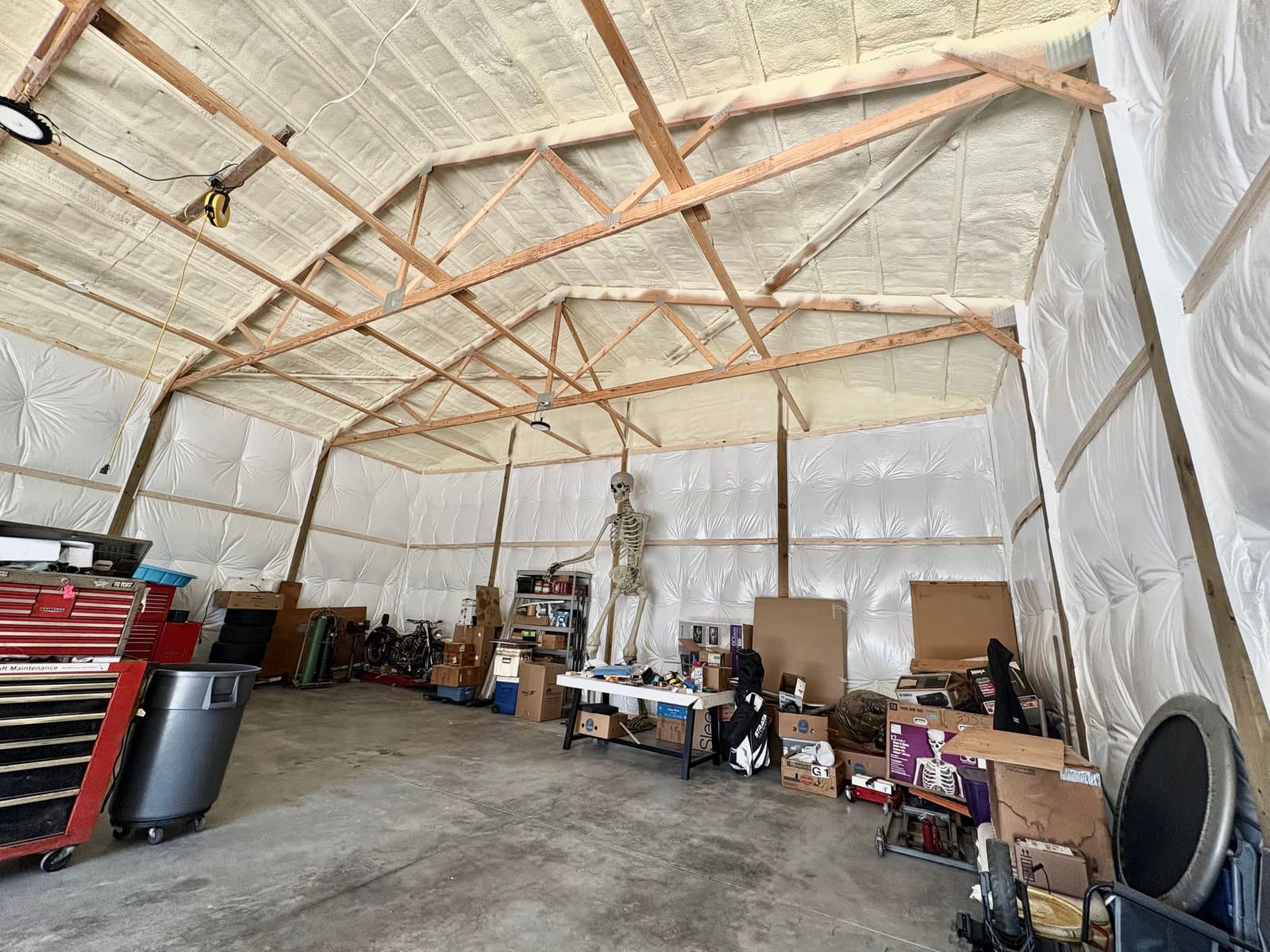 Pole barn workshop with spray foam insulation covering the underside of the roof between the wooden trusses and white faced insulation lining the sidewalls