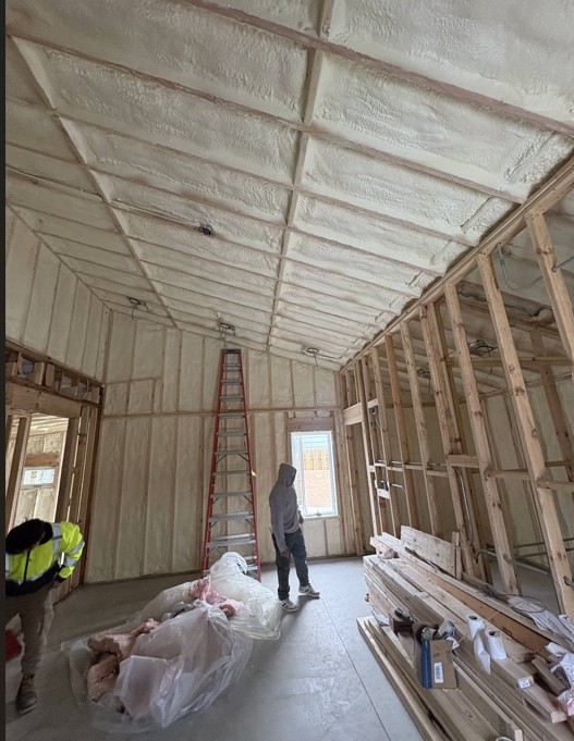Spray foam insulation covering the vaulted ceiling and exterior walls of a house under construction near Elgin, IL, with a step ladder and stacked lumber still in the room