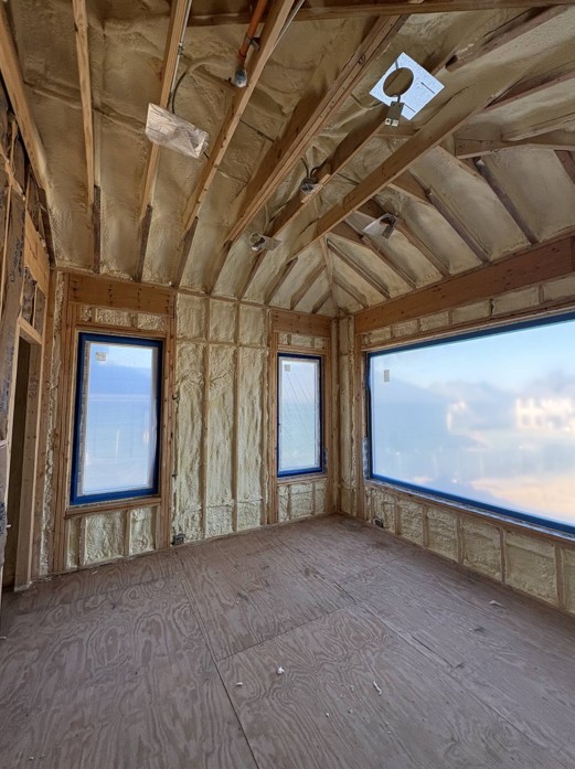 Spray foam insulation applied between the exposed rafters and around the windows of a timber framed room near Elgin, IL, with a large picture window and a plywood subfloor